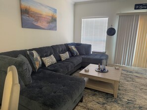 Ein Wohnzimmer mit einem dunkelgrauen Ecksofa, einem Couchtisch und einem Gemälde einer Strandlandschaft.