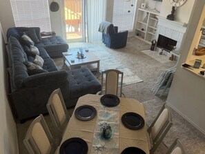 Ein Wohnzimmer mit einer Eckcouch, einem Esstisch für vier Personen und einem Kamin.