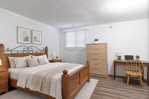 A bedroom with a wooden bed, a desk, a chair, and a wardrobe. - Surrey-Langley-Luxurious Suite | Prime Location & Ultimate Comfort (Langley)