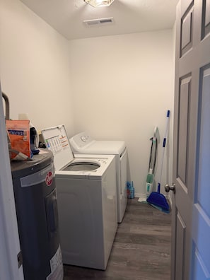 A laundry room with a front-loading washer and dryer, a vacuum cleaner, and cleaning supplies.