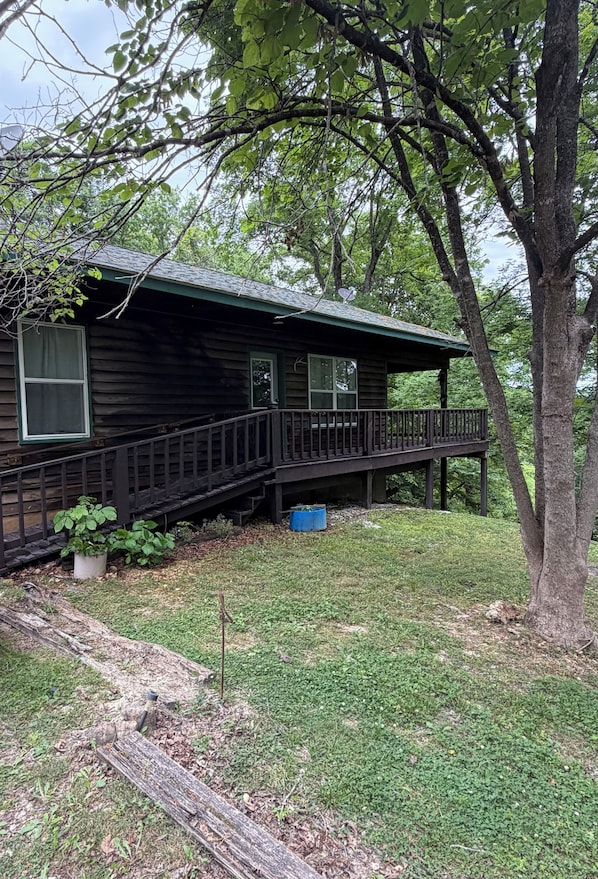 A wooden cabin with a porch, surrounded by trees and grass.