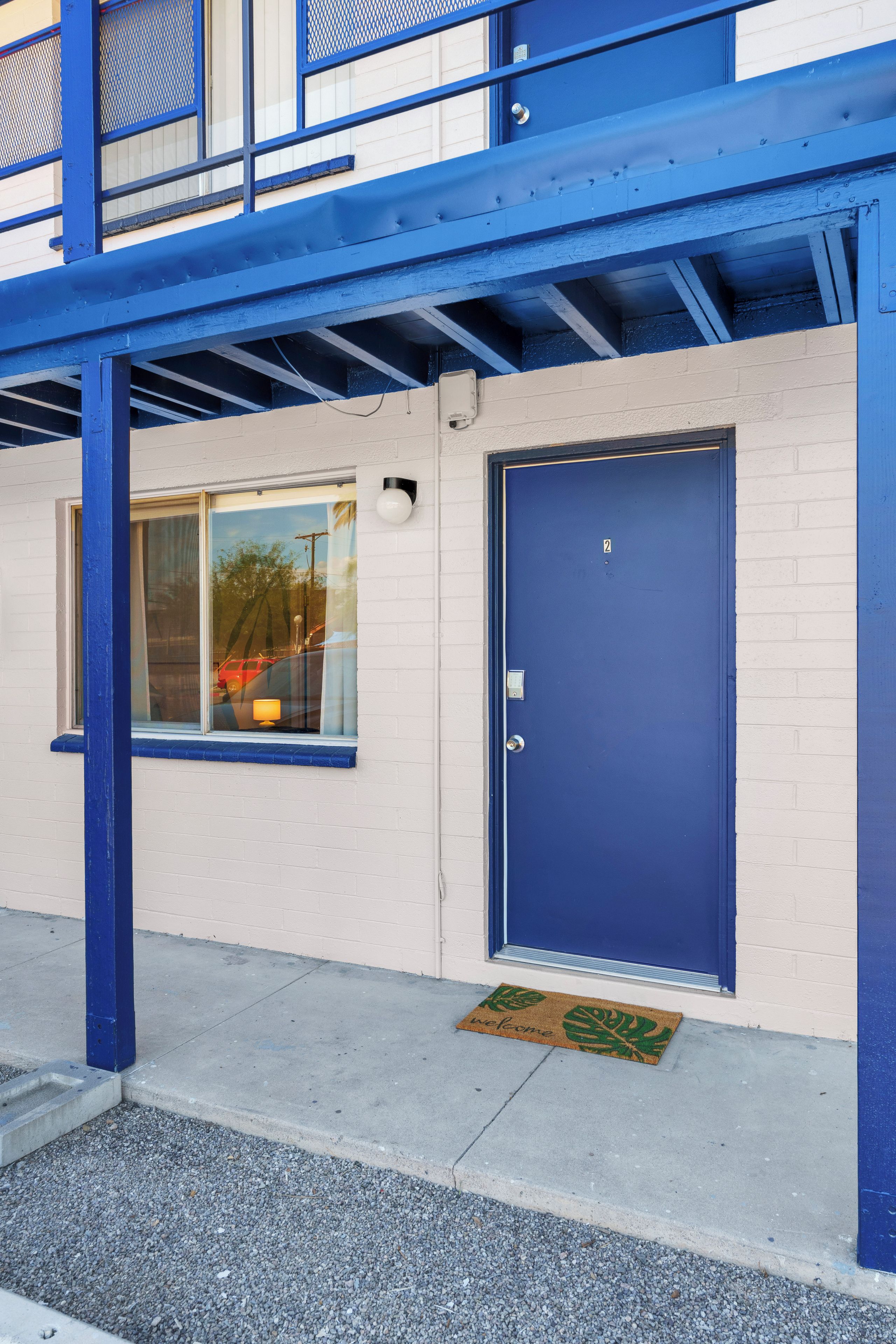 A building with a blue door and window, a doormat, and a metal structure above.