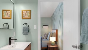 Une salle de bain moderne avec un meuble-lavabo en bois, un miroir et deux œuvres d’art encadrées accrochées au mur.