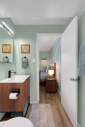 Ein modernes Badezimmer mit einem Holzkosmetikschrank, einem Spiegel und zwei gerahmten Kunstwerken an der Wand.