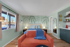 Ein Schlafzimmer mit einem Bett, einem Nachttisch, einem Sessel, einem Fenster mit Vorhängen und einer Wand mit einem Blattmuster.
