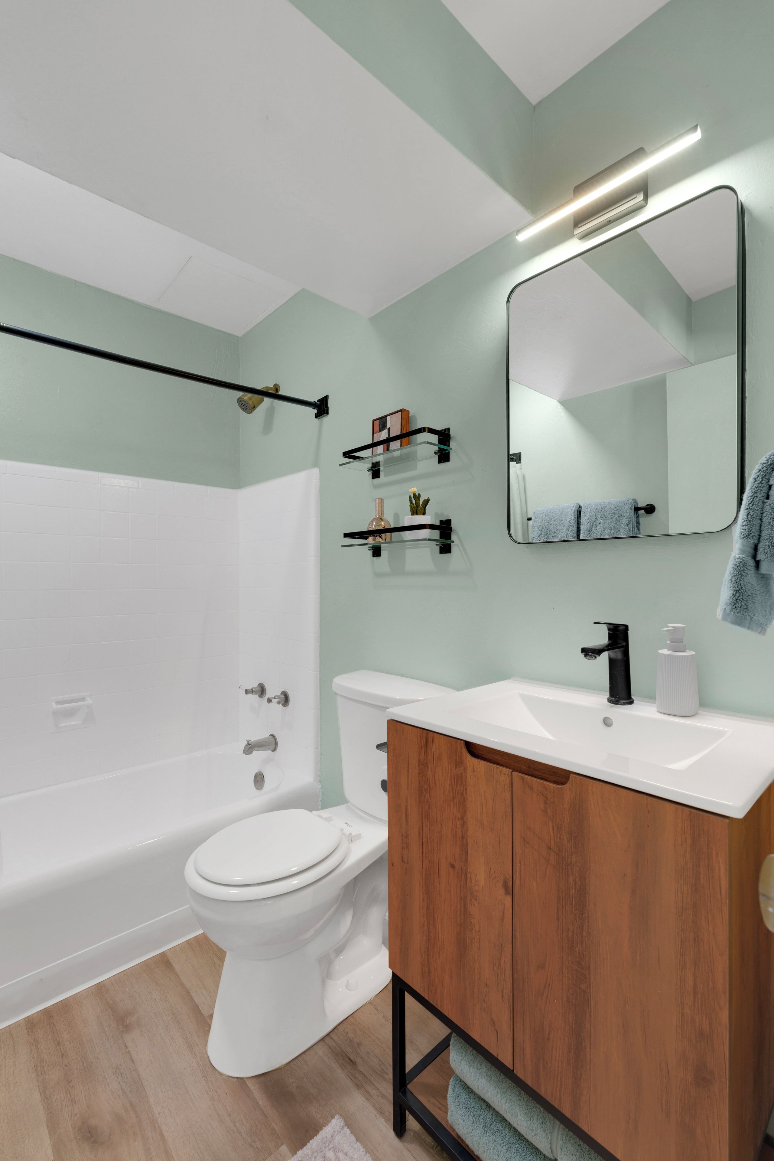 A modern bathroom with a white toilet, a wooden vanity, a mirror, and a shower area.