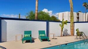 Un espace aménagé au bord de la piscine, avec deux fauteuils de jardin verts, un mur en briques blanches et une piscine à l’eau d’un bleu limpide.