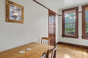 Ein Esszimmer mit einem Holztisch, Stühlen, einem gerahmten Bild an der Wand und einem Fenster mit Blick auf Grünflächen.