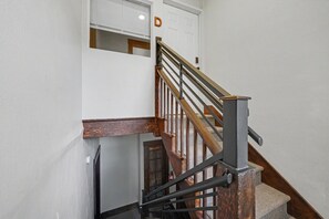 Eine Treppe mit Holzbodenstufen und einem Metallgeländer, die zu einer weißen Tür mit dem Buchstaben 'D' darüber führt.