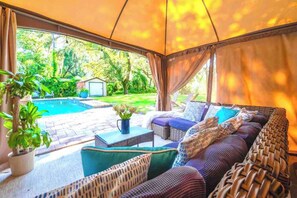 A covered outdoor seating area with a pool view, wicker furniture, and a potted plant. - Riverfront Retreat | Sleeps 14 | Pool | Spa | Deck (Tampa)