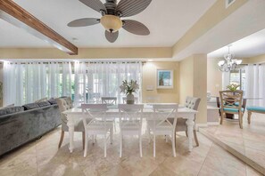 A dining area with a table and chairs, a ceiling fan, and a sofa in a room with large windows and curtains. - Riverfront Retreat | Sleeps 14 | Pool | Spa | Deck (Tampa)