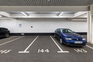 Uma garagem de estacionamento com vagas demarcadas e um carro azul estacionado em uma delas.