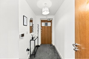 A hallway with a wooden door, a framed certificate on the wall, a small table with a plant, and a ceiling light fixture. - Luxury Flat • City Centre • Balcony • FreeParking • Fast WiFi • Work Desk • SmartTVs • Yoko Property (Milton Keynes)
