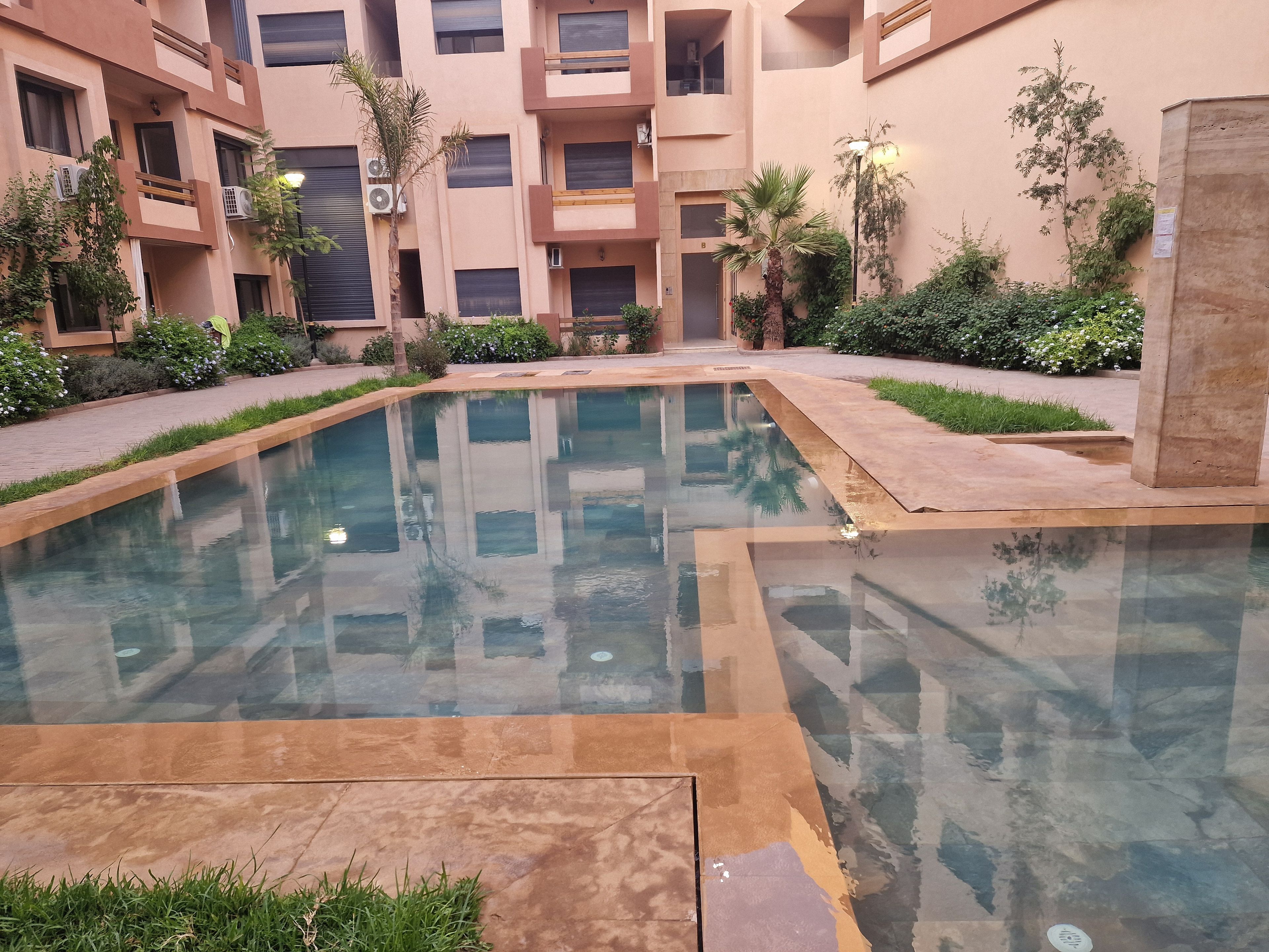 Une cour intérieure avec une piscine centrale, entourée d’immeubles à plusieurs étages dotés de balcons et de climatiseurs.