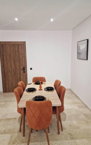 A dining area with a wooden table and six chairs, a door, and a framed picture on the wall. - Beautiful  apartment with pool & security in central Marrakesh (Marrakesh)
