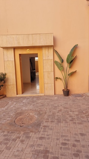 A building entrance with a brick-paved courtyard, a potted plant, and a manhole cover. - Beautiful  apartment with pool & security in central Marrakesh (Marrakesh)