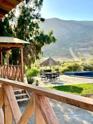 Une terrasse en bois avec une table et des chaises, une piscine et une vue sur un paysage montagneux.
