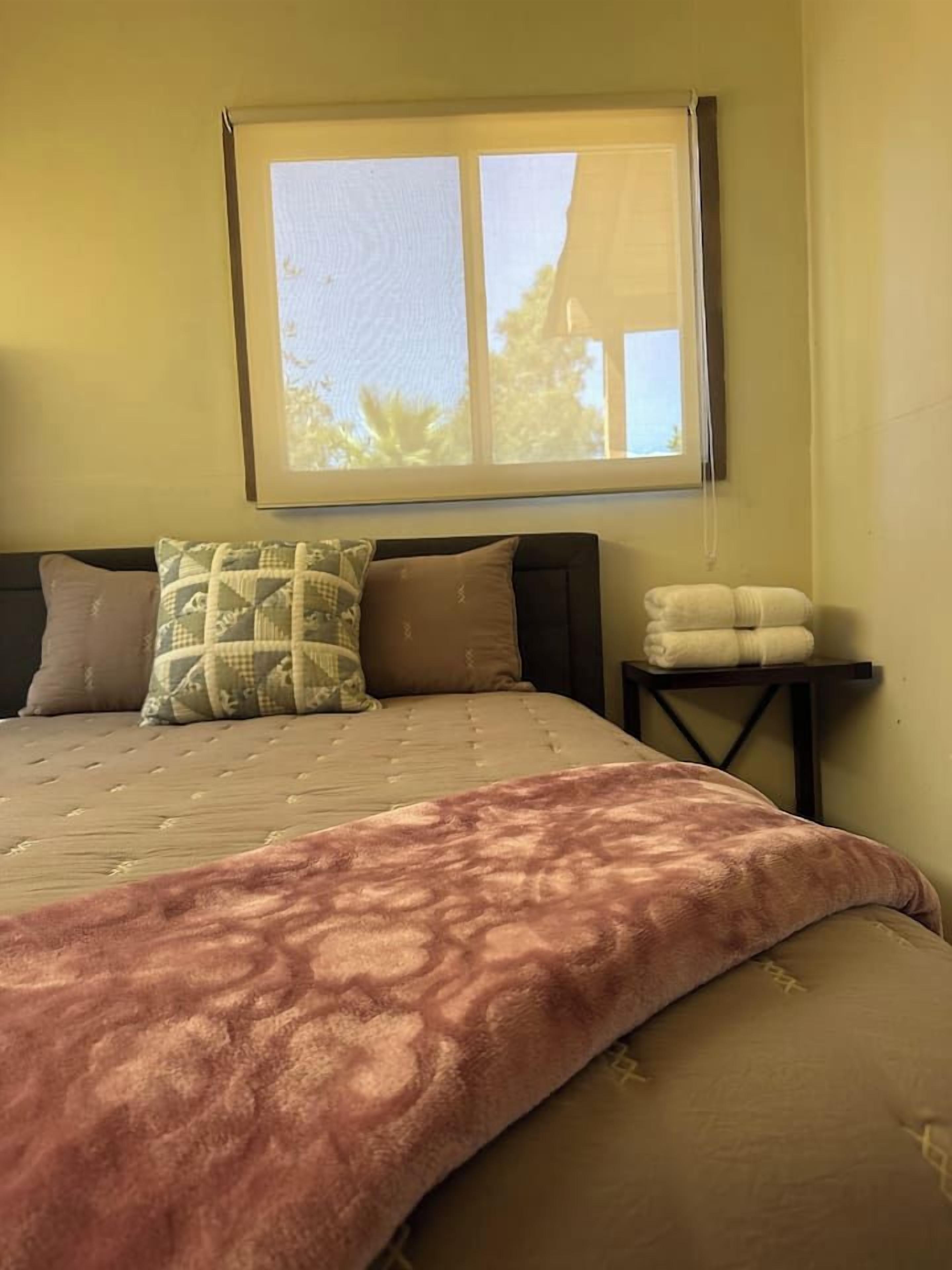 A bed with a patterned bedspread, pillows, and a bedside table with towels.