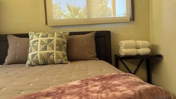 A bed with a patterned bedspread, pillows, and a bedside table with towels.