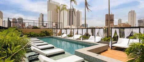 A rooftop pool area with lounge chairs and a view of the city skyline.