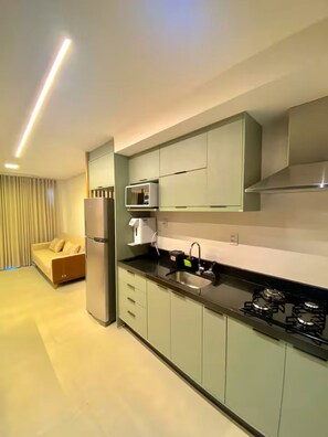 A modern kitchen with a built-in microwave, a gas stove, and a refrigerator. - Premium Apartment in Setor Bueno | Full-Service Condominium with Heated Pools (Goiânia)