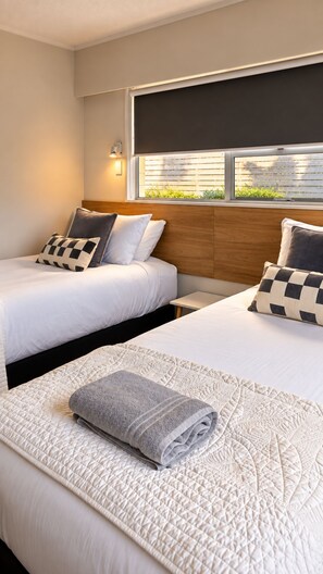 A hotel room with two beds, a window with blinds, and a view of greenery outside. - Love It on Lemon | Stay Central | Explore More! (New Plymouth)