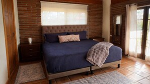 A bedroom with a large bed, a wooden headboard, a nightstand, a window with blinds, and a door leading outside. - Quinta Aurora - Relaxing Wine Country Casa w/Pool (San Marco)