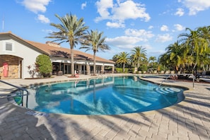 A swimming pool with a curved edge, surrounded by palm trees and a building with a tiled roof. - 3BR/3BA · Private Heated Pool · Gated Resort · Near Venice & Gulf Beaches (Nokomis)
