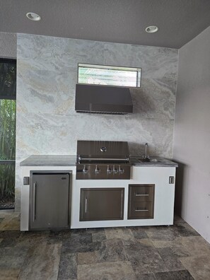 A modern kitchen with a built-in stove, oven, and sink, featuring a marble backsplash and a small refrigerator. - 3BR/3BA · Private Heated Pool · Gated Resort · Near Venice & Gulf Beaches (Nokomis)