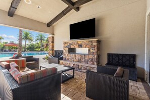 Une terrasse extérieure avec une cheminée en pierre, des meubles en osier et un téléviseur à écran plat.