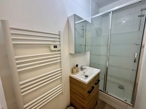 A bathroom with a glass shower enclosure, a white sink, and a wooden cabinet. - Two-bedroom apartment with a view of the Seine, 1 km from the train station (Melun)