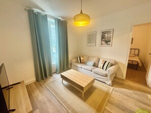 A living room with a sofa, a coffee table, a hanging light fixture, and a window with curtains. - Two-bedroom apartment with a view of the Seine, 1 km from the train station (Melun)