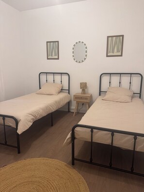 A room with two single beds, a small wooden nightstand, a mirror, and two framed pictures on the wall. - Two-bedroom apartment with a view of the Seine, 1 km from the train station (Melun)