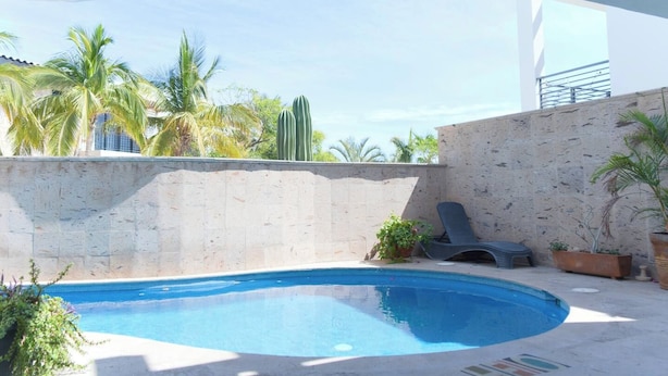 A swimming pool with a curved edge, surrounded by a stone wall and potted plants. - Tranquil Cabo Villa w/ Private Pool, Grill & Patio (Cabo San Lucas)