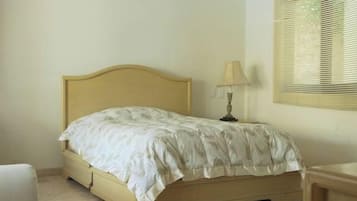 Una camera da letto con un letto, una ventola a soffitto, un comodino con una lampada e una finestra con persiane.