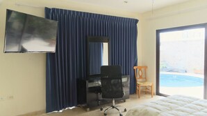 A hotel room with a bed, a desk with a chair, a TV mounted on the wall, and a view of an outdoor swimming pool. - Tranquil Cabo Villa w/ Private Pool, Grill & Patio (Cabo San Lucas)