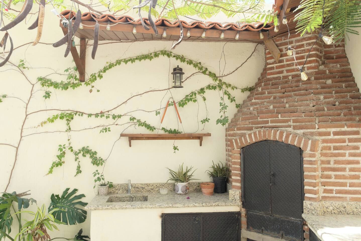 Eine Terrasse mit Lehmofen, Kübelpflanzen und einer Hängelampe.