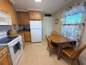 A kitchen with wooden cabinets, a white refrigerator, a stove, and a dining table with chairs. - Quaint 2-bedroom bungalow, close to the ocean in charming Thomaston (Thomaston)