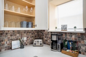 A kitchen with a coffee bar, a toaster, a coffee maker, and a basket of coffee bags. - Casa Marina ✨ Spacious 3BR • 1 Mile to Pearl & Downtown (San Antonio)