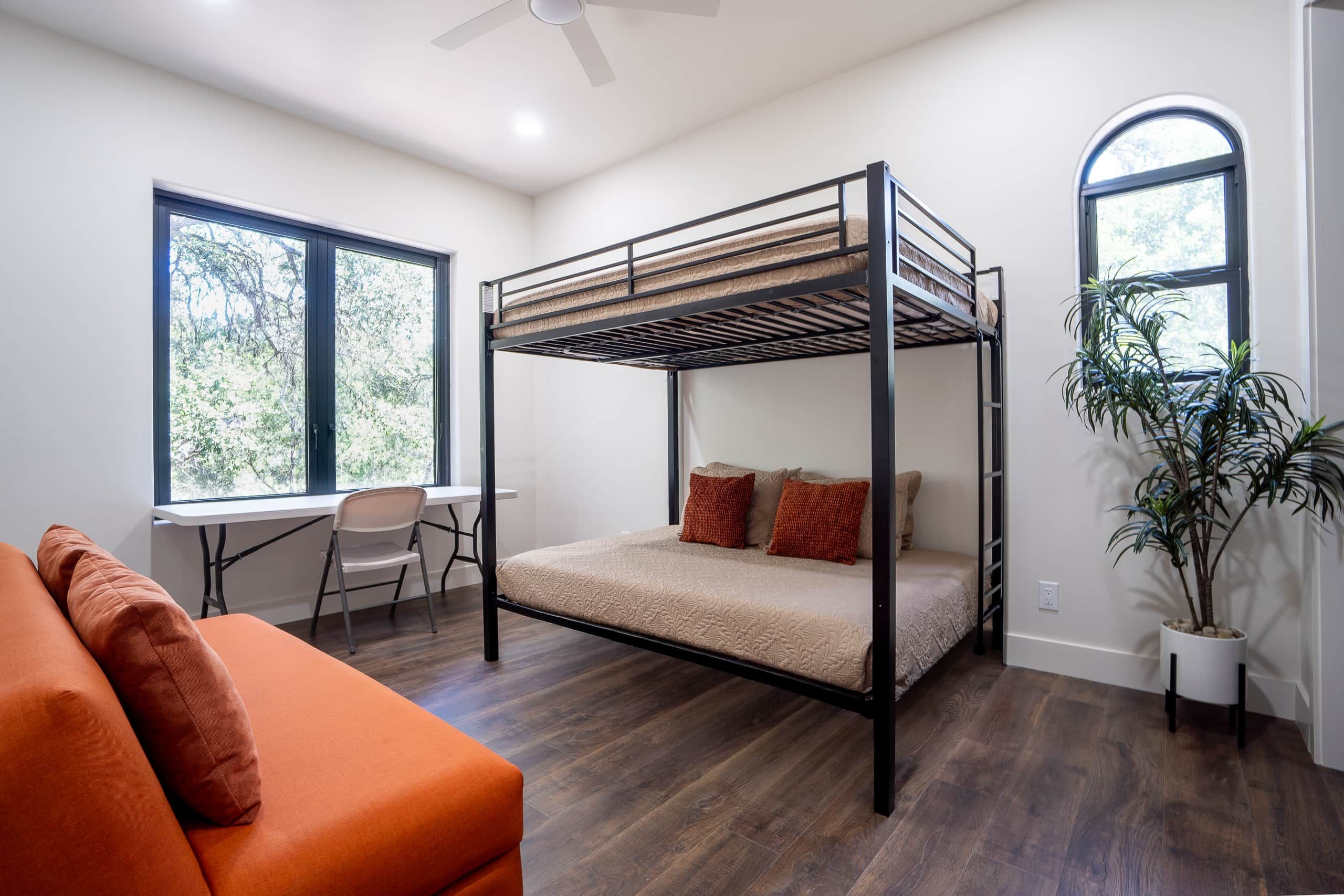 A bunk bed room with a desk, chair, and a potted plant.
