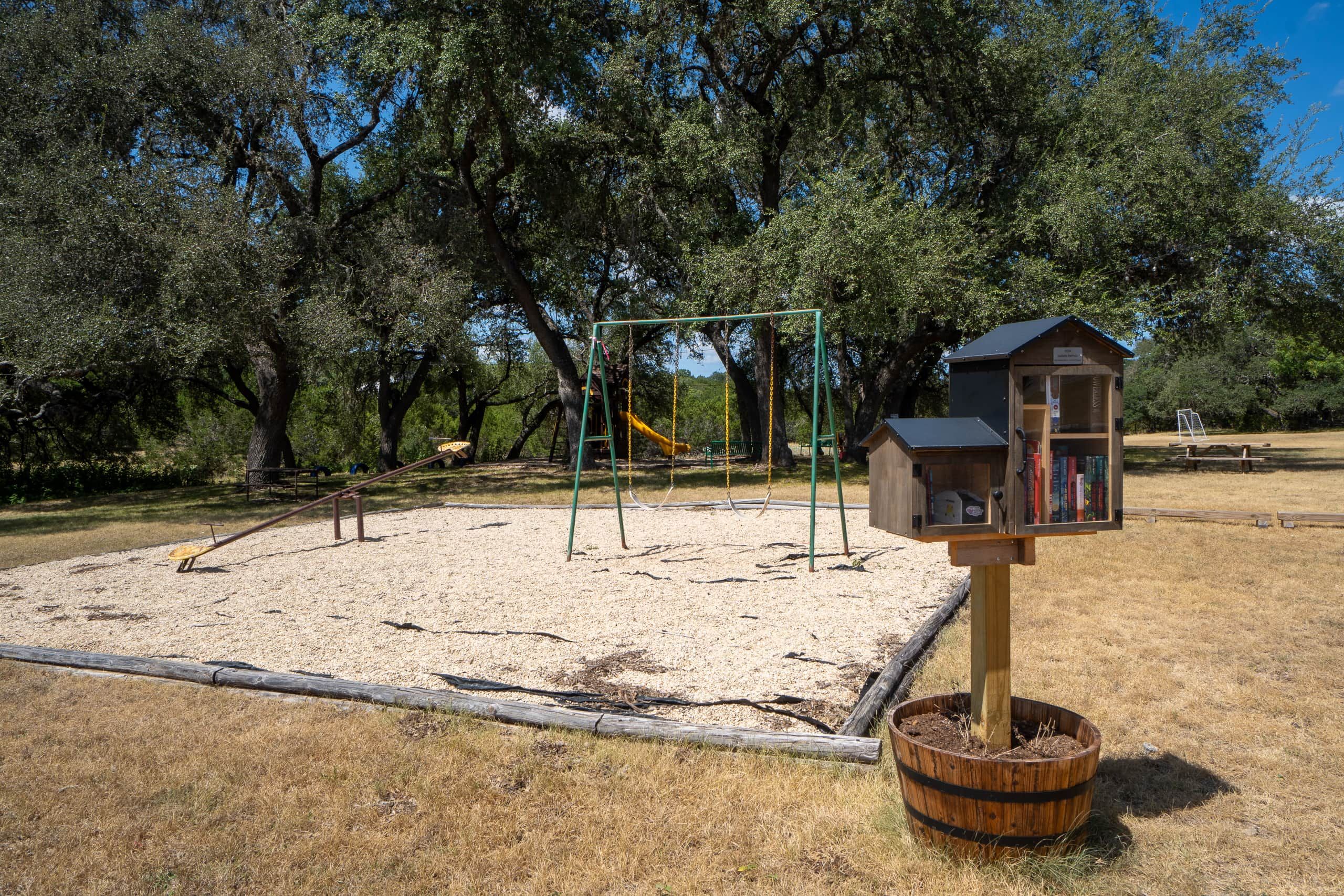 A playground with swings and a slide, surrounded by trees.