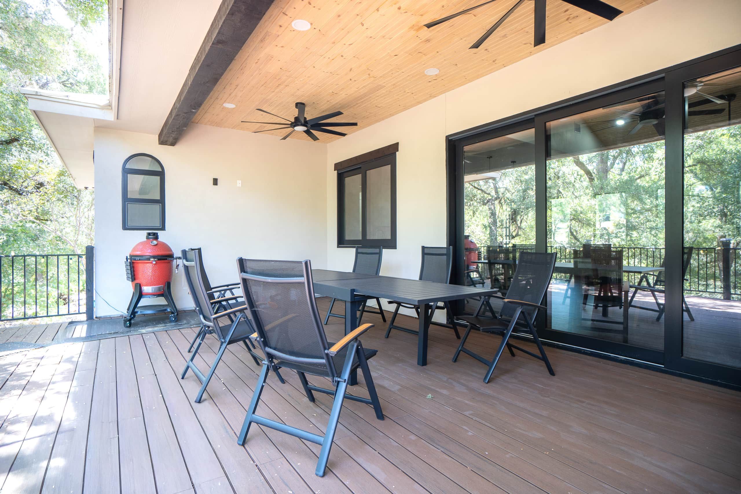Un patio exterior con cubierta de madera, ventilador de techo y una parrilla.
