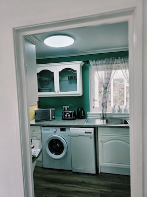 Une cuisine compacte équipée d’un lave-linge, d’un four à micro-ondes et d’une machine à café.