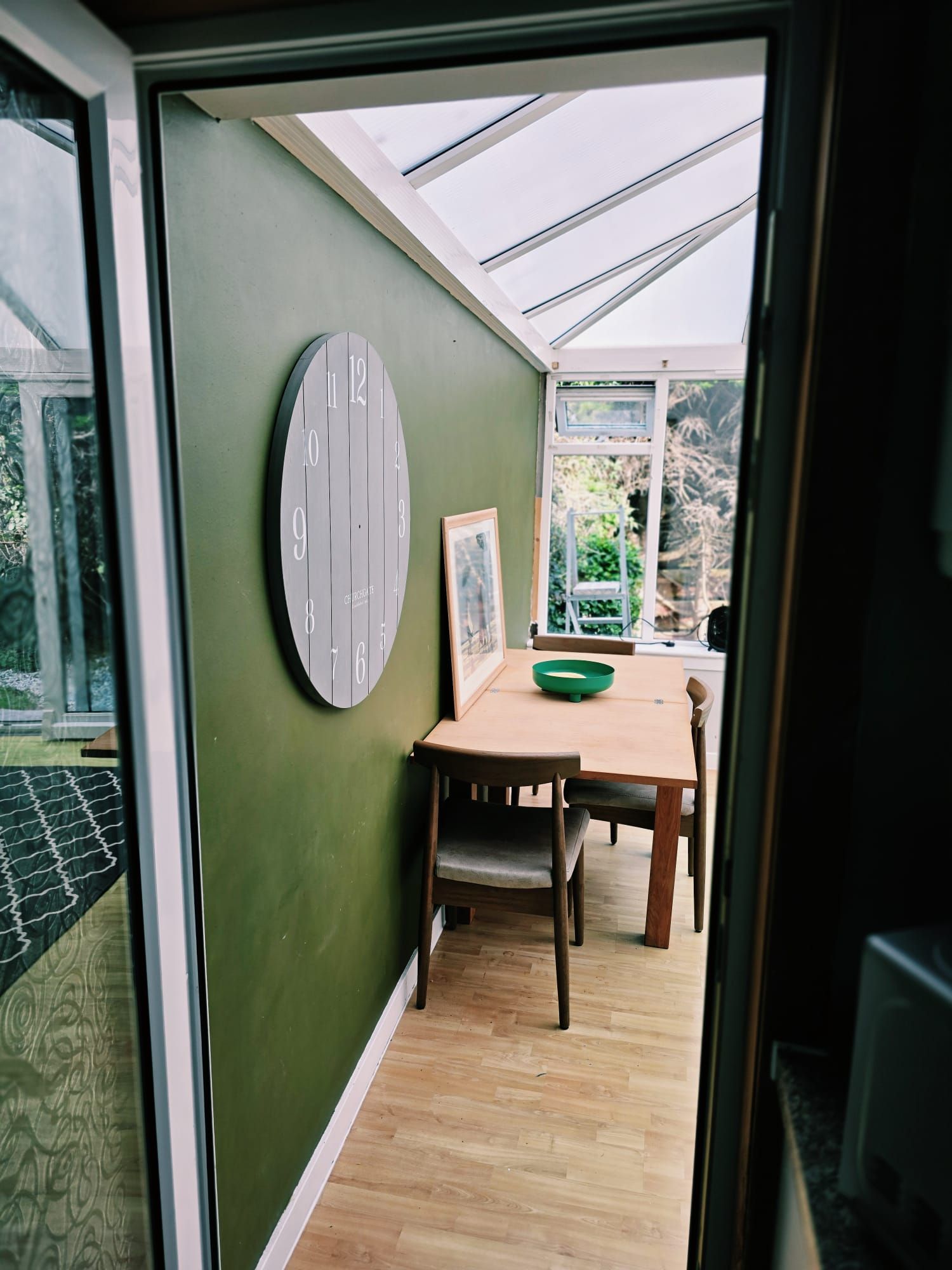 Una habitación con una mesa de madera, una pared verde y un reloj grande.