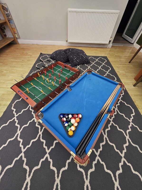 A room with a foosball table, a pool table, and a radiator.