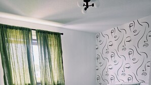 Un dormitorio con cama, una ventana con cortinas verdes, cabecera estampada y piso alfombrado.