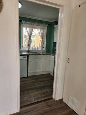 A kitchen with white cabinets, a window with curtains, and a wooden floor.