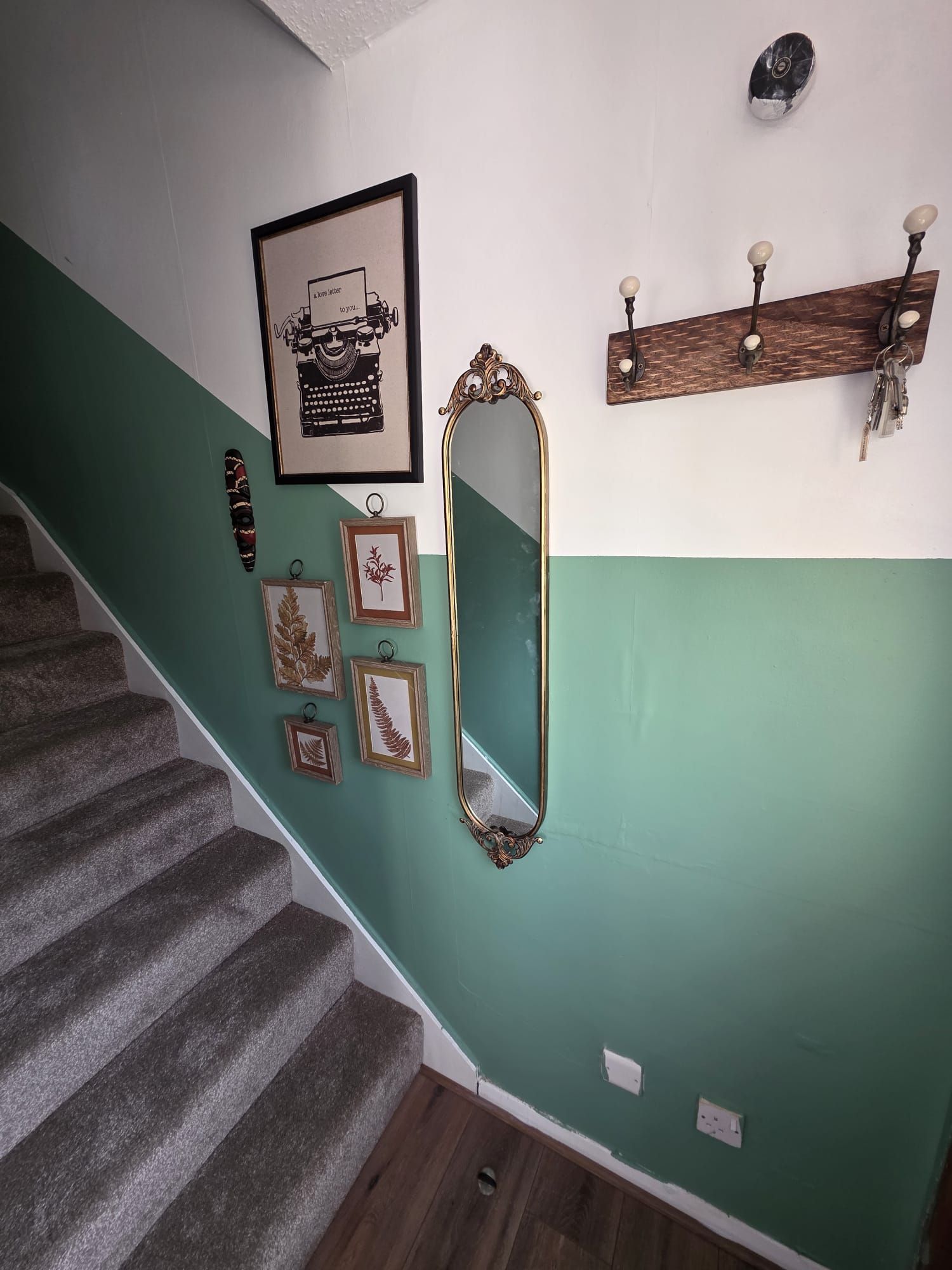 A staircase with a green wall, a framed typewriter, a mirror, and a coat rack with keys.