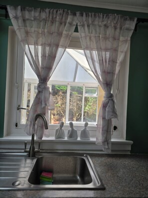 A kitchen with a sink, a window with curtains, and a view of trees outside.
