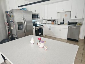 A modern kitchen with white cabinets, stainless steel appliances, and a central island with a teapot and cup. - Cozy 1-bedroom for rent in pleasant St. Petersburg with AC (St. Petersburg)